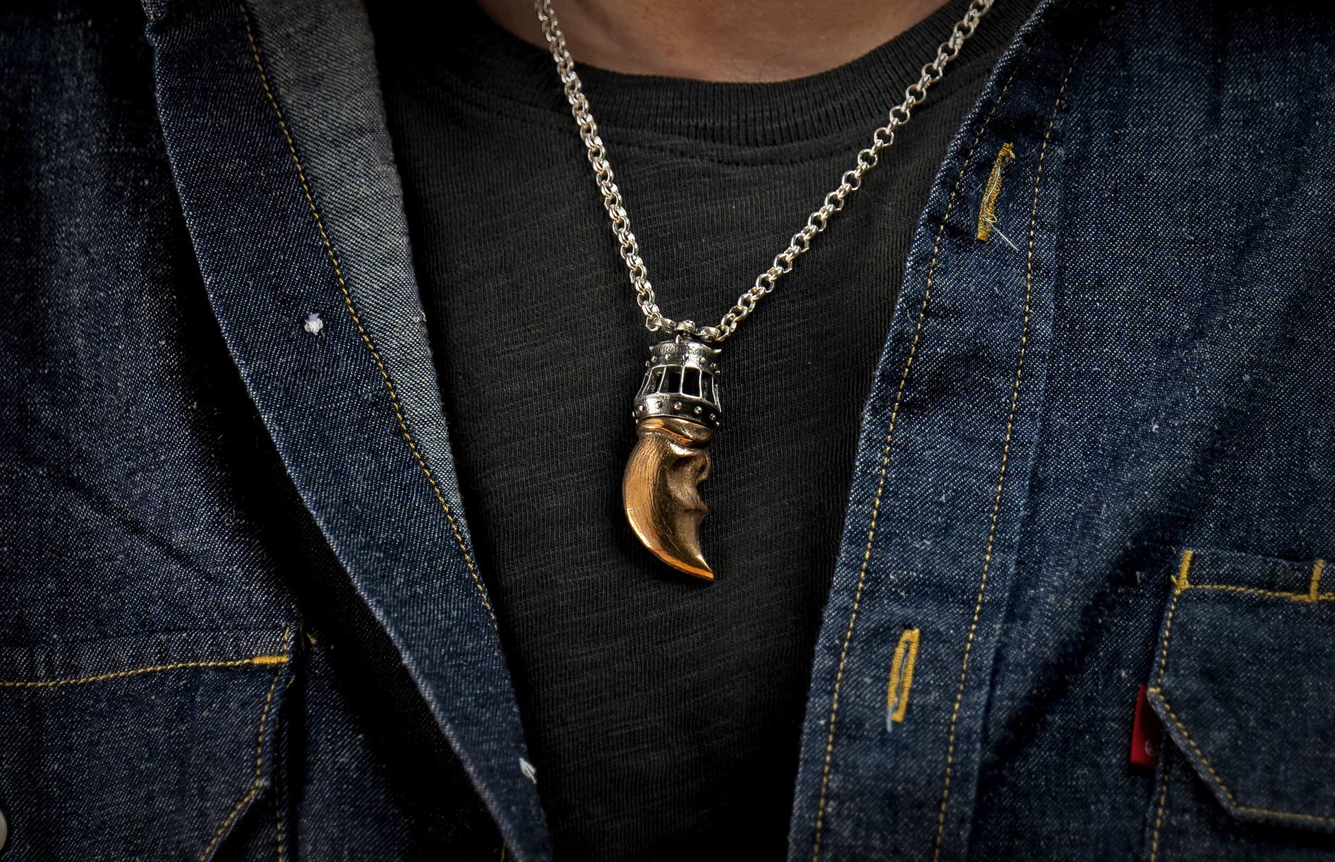 Golden and silver-toned claw pendant necklace worn over a black t-shirt and denim jacket.