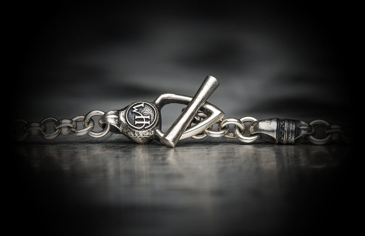 Silver-toned metal bracelet with a textured toggle clasp, featuring circular detail with "WH" initials and thick chain links.