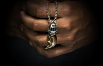 King's Claw pendant necklace with a bronze-toned claw and silver cap on a silver chain, held by hands.
