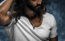 King's Claw pendant with a silver cage and dark brown claw, on a silver chain worn by a man in a white t-shirt.