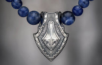 Sodalite shield pendant necklace in silver and blue sodalite, with intricate etched details.