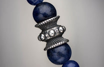 Ornate metal Sodalite Shield bead featuring ridged patterns and spherical accents, surrounded by deep blue sodalite beads.