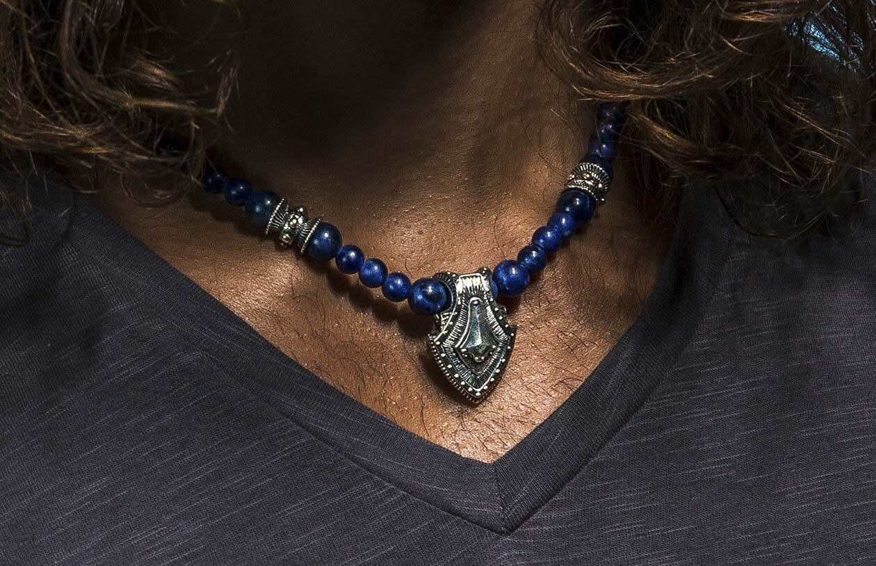 Sodalite shield necklace with blue beaded stones and a silver-toned shield pendant, worn on a person's neck.