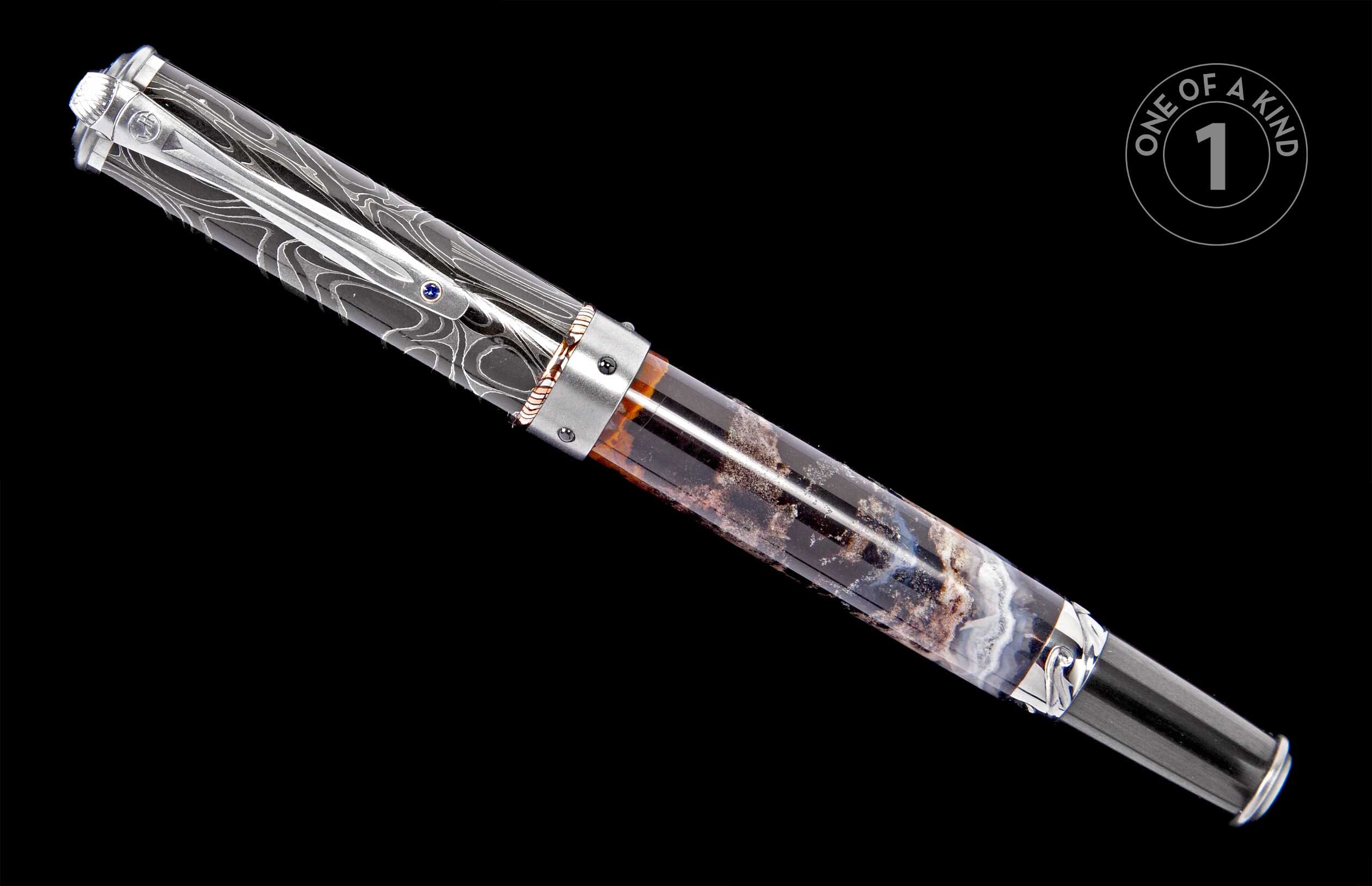 Luxury pen with a silver Damascus-patterned cap, blue gem, and translucent barrel of swirling brown and white resin, angled diagonally.