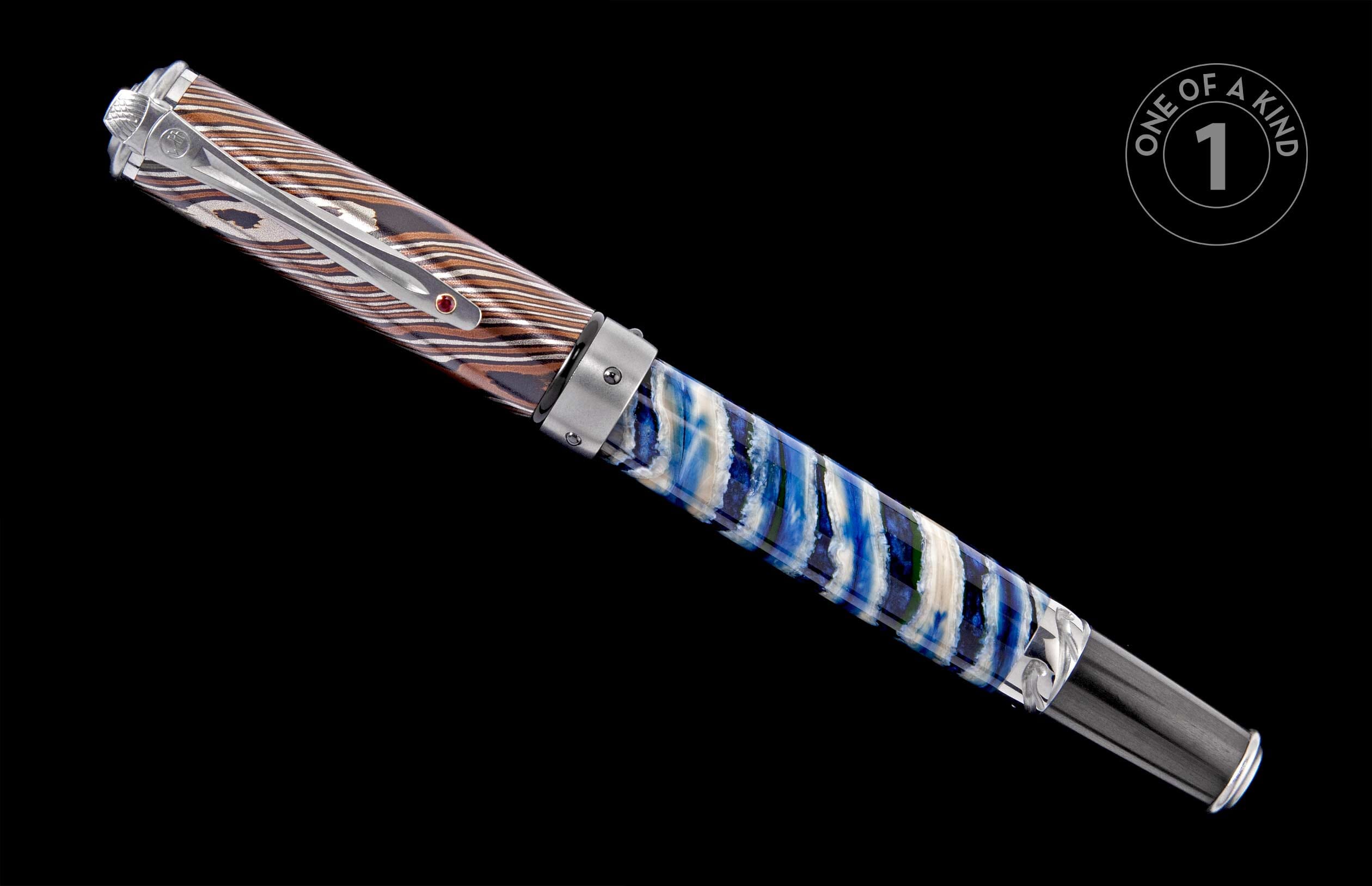Pen with a damascus-patterned cap in silver and brown, and a swirled blue, white, and green resin barrel with a silver clip and red gem.