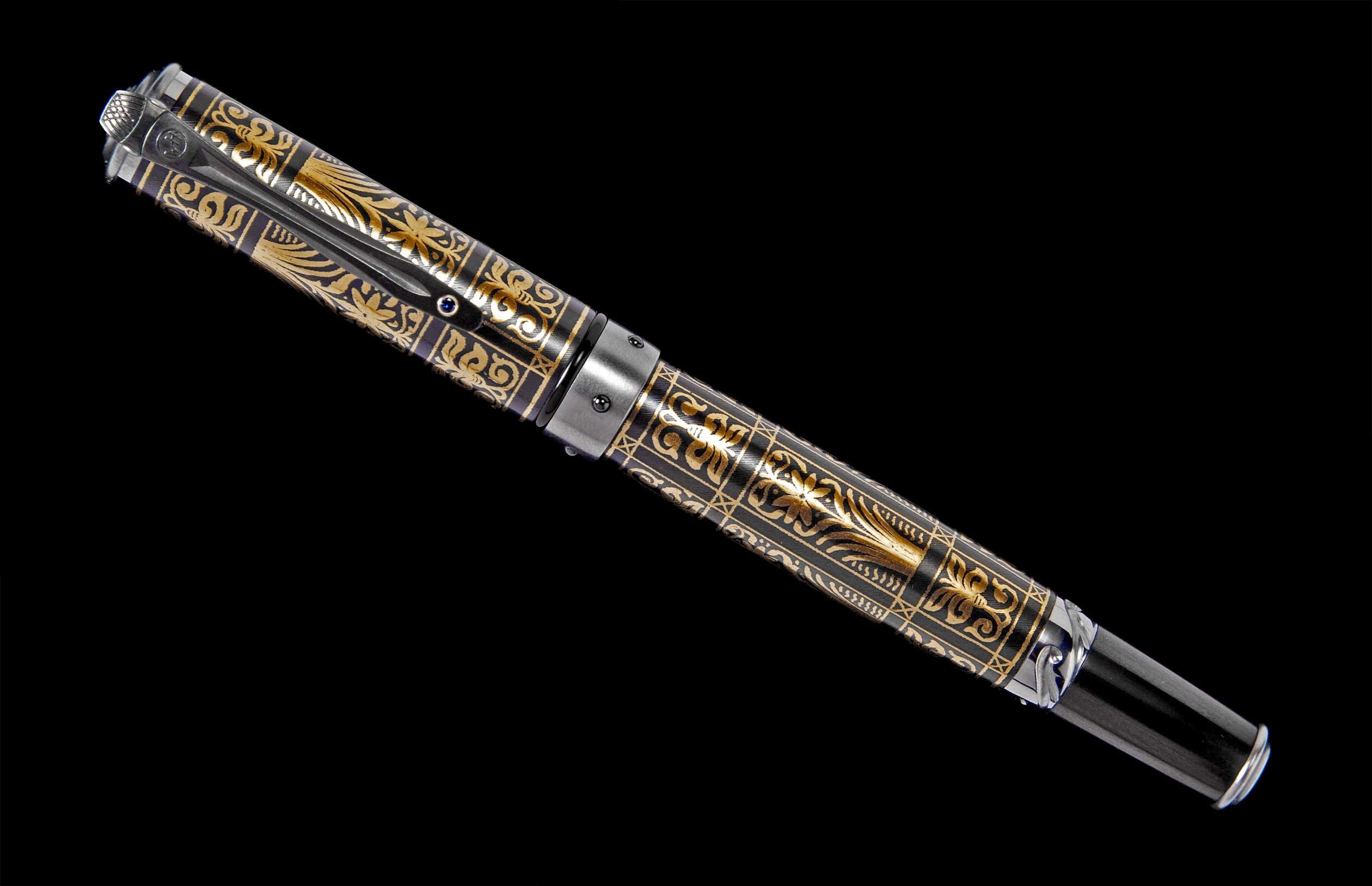 Black and gold ornate pen with intricate scrollwork patterns and a blue gem on the clip, displayed diagonally.