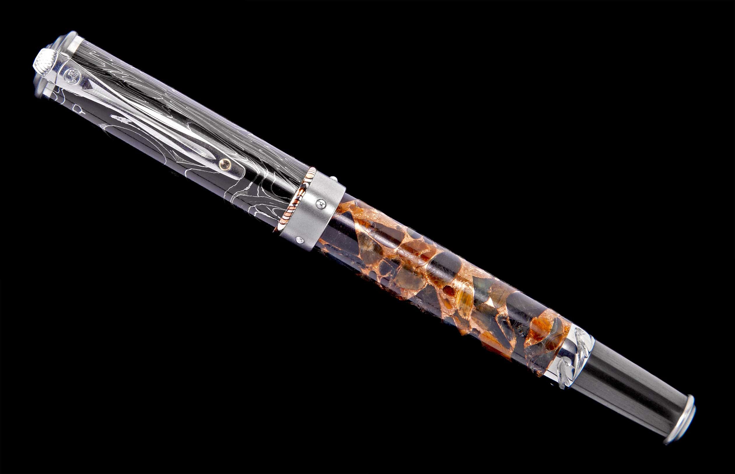 Black and silver fountain pen with a unique barrel featuring embedded amber-colored fragments, and a cap with white swirling patterns.
