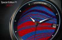 Luxury Fordite dial watch by William Henry with vibrant red and blue marbled texture, polished silver hands, date window, and faceted bezel in close-up view