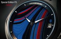 Special Edition Fordite watch by William Henry featuring blue, red, and black striped dial with textured finish, silver-toned hands, and triangular hour markers, close-up front view