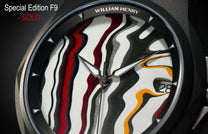Special Edition Fordite watch by William Henry featuring swirling red, black, white, and gold marbled dial with silver triangular hour markers and date window, close-up front view