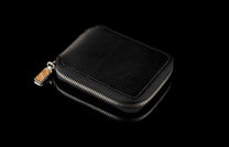 ZBF LIZ BLK MT|Black leather zipper bi-fold with a textured finish and a patterned stone zipper pull, reflected on a dark surface.