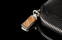 ZBF LIZ BLK MT|Black leather zipper bi-fold with scales texture, silver zipper, and a rectangular brown and white striped stone pull, reflected on a dark surface.